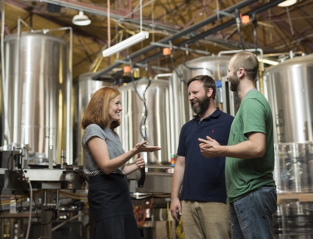 Three people talking in front of brewery production line